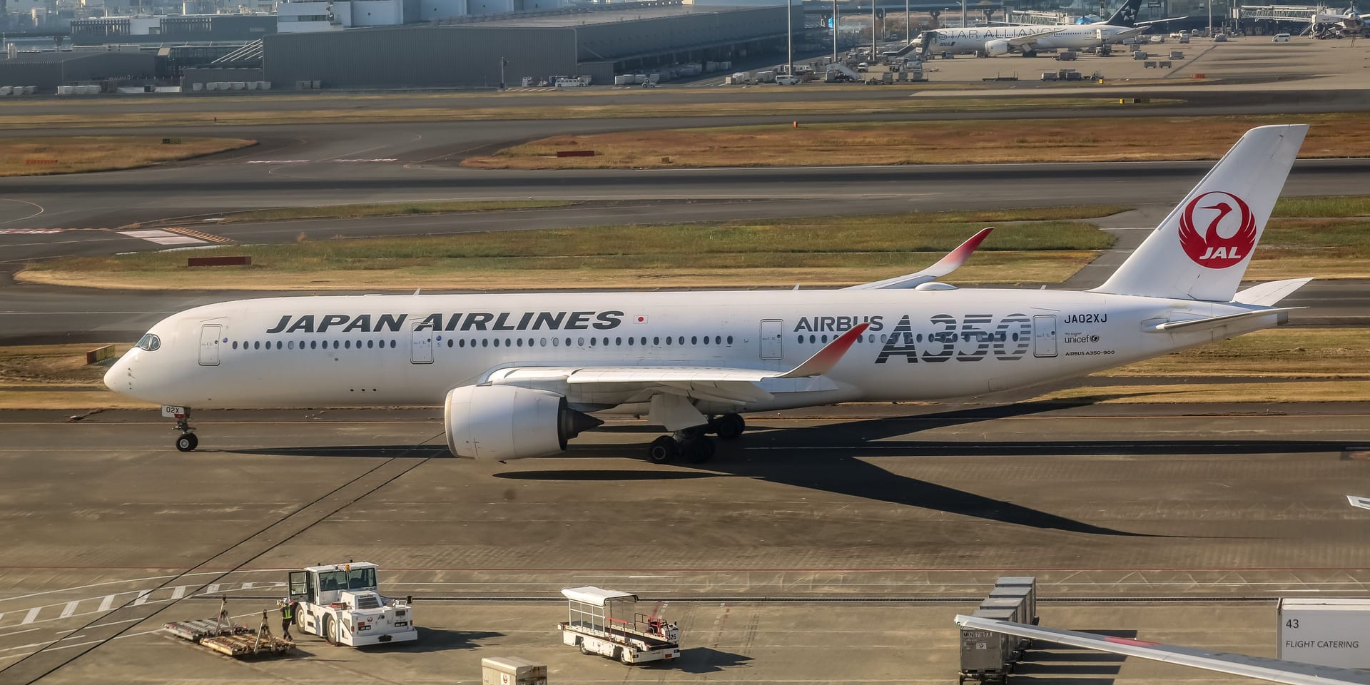 A Japan Airlines Airbus A350 taxiing at Haneda Airport with the Tokyo skyline visible in the background